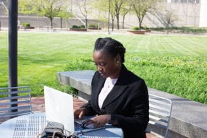 Moyo works at a laptop at an outdoor table.
