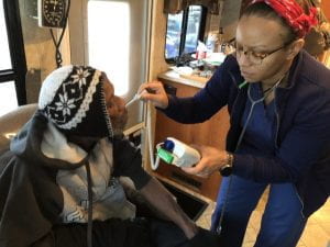 A clinic worker takes the temperature of a Black woman sitting in a mobile clinic.