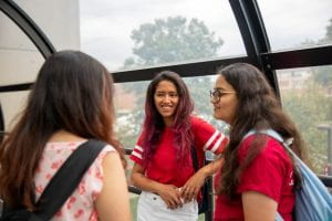 Unnati and two friends stand talking by a window on campus.