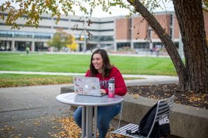 Nerea sits at an outdoor table on campus working on her laptop.