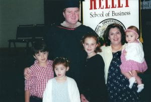 Jason stands with his family in his cap and gown. He's with his wife and three young children.